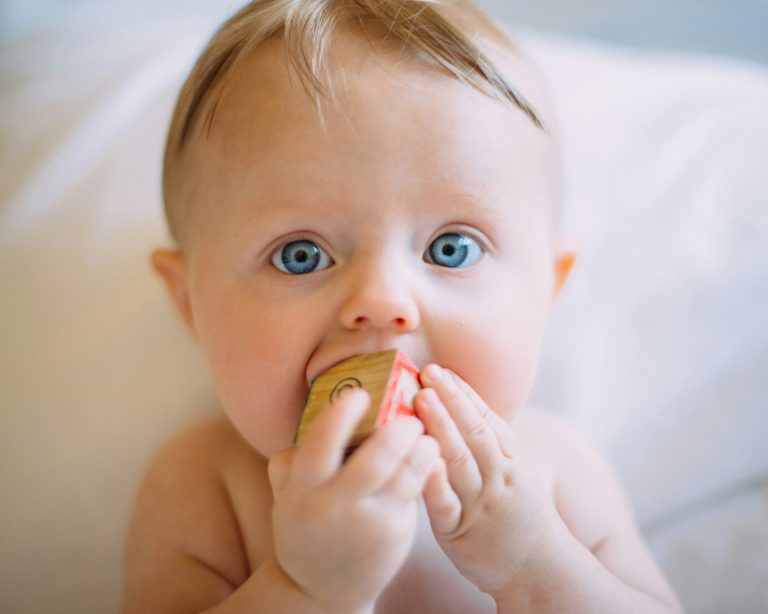 Un bébé aux yeux bleu met dans sa bouche un cube.