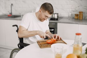 un homme en fauteuil roulant coupe des légumes dans sa cuisine adaptée aux PMR