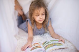 une enfant lit un livre en FALC. Elle est couchée sur le ventre dans un lit pour lire