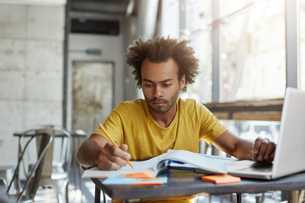 Un homme étudie devant son ordinateur et ses livres de cours pour valider sa formation en vue de travailler avec des enfants handicapés