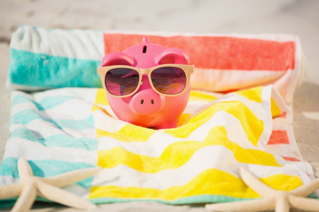 un cochon en tirelire rose avec des lunettes de soleil sur une serviette de plage pour représenter les aides financières pour des vacances accessibles aux personnes handicapées